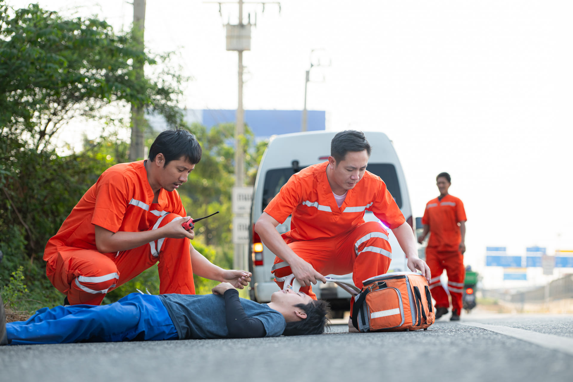 Paramedics assisting injured person on roadside near ambulance